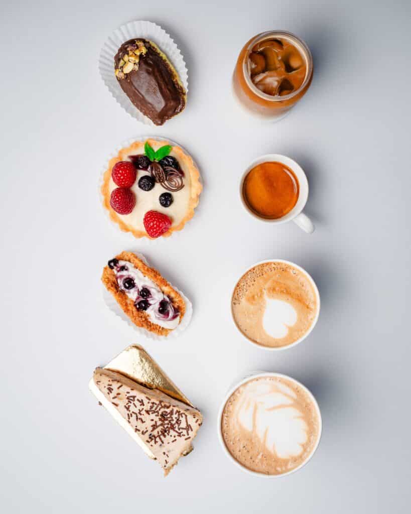 A variety of coffee drinks and pastries from Aurora Coffee Hub, including lattes, espresso, fruit tarts, and chocolate eclairs.
