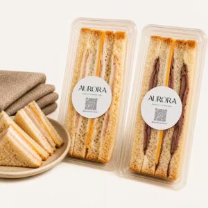 Two packaged club sandwiches with Aurora branded stickers next to sliced triangle finger sandwiches on a plate.